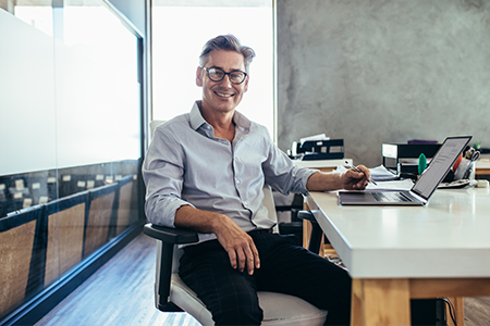 smiling male business owner sitting at desk with laptop