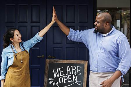 smiling male and female cafe owners sharing a high-five over their We are Open sign