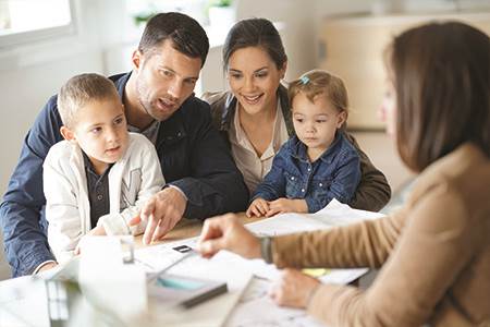 husband and wife with young son and daughter sitting at desk reviewing loan documents with a mortage lender