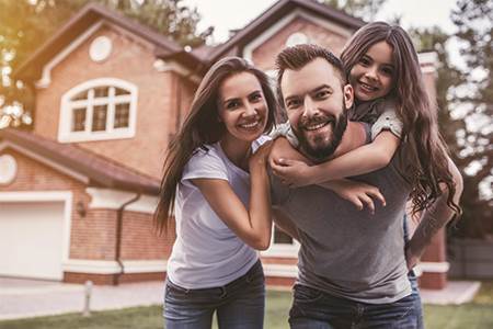 excited man, woman, and young girl with arms around each other infront of their new brick home