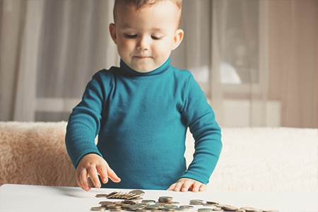 young boy in at coffee table in living room counting out coin to become a Juinor Money Master