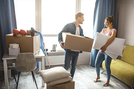 happy man and woman standing in living room unpacking moving boxes