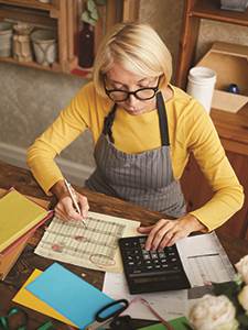 senior female business owner sitting at desk with calculator balancing business receipts