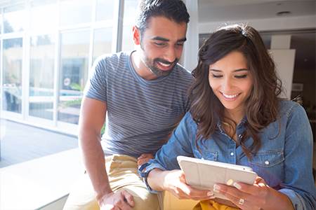 happy man and woman sitting together looking at marine bank mortgage rates on mobile device