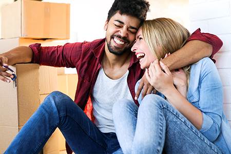 laughing happy man holding new house keys and woman sitting on the floor surrounded with moving boxes