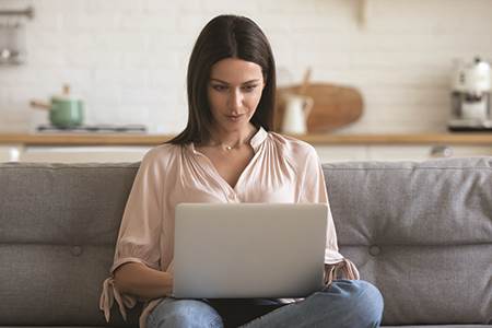 Woman on couch on laptop looking at checking accounts