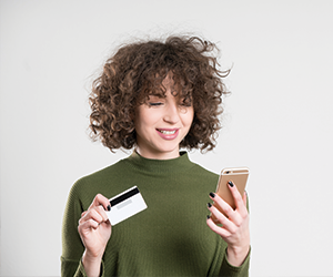 happy woman holding mobile device in one hand and a debit card in the other hand