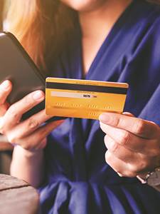 female holding credit card in one hand and holding mobile device in another