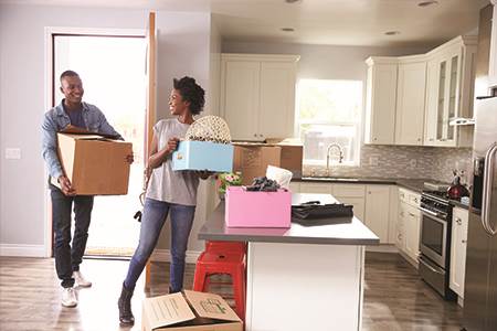 happy young man and woman carrying moving boxes into new kitchen