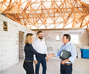 smiling male and female business owners shaking hands with male commercial real estate agent while in new building space